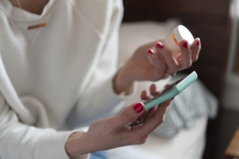 Woman holding smart phone and pill bottle