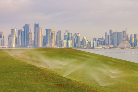Sprinkler system on lawn by skyline of Doha, Qatar