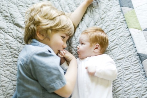 View directly above boy with his baby brother lying on bed