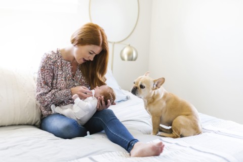 Dog sitting by woman holding her newborn son on bed