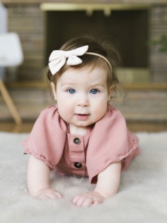 Baby girl wearing bow hair band lying on rug