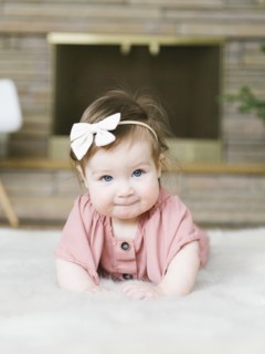 Baby girl wearing bow hair band lying on rug
