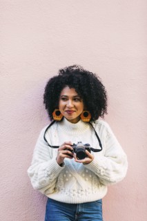 Young woman holding camera against pink wall