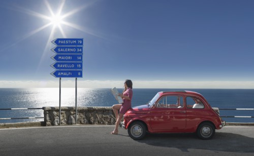 Woman holding map leaning on pink car