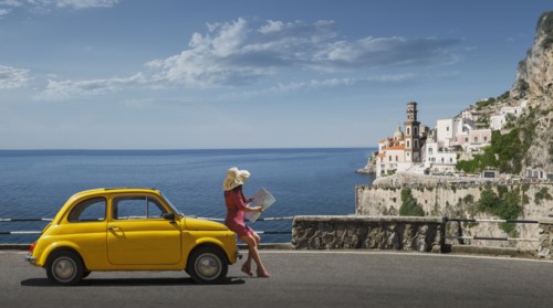 Woman holding map leaning on yellow car in Atrani, Italy
