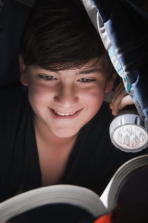 Boy reading with torch under blanket