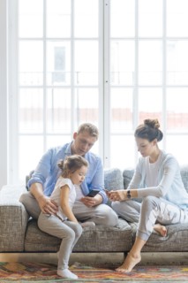 Parents holding smart phones on sofa with their daughter