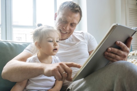 Father reading book to daughter on sofa