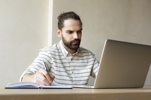 Young businessman with laptop writing in note pad