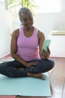 Mature woman with smart phone sitting on yoga mat