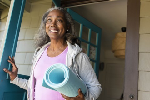 Smiling woman with yoga mat front door