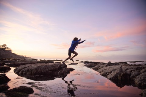 Teenage boy jumping between rocks of tide pool in La Jolla, California