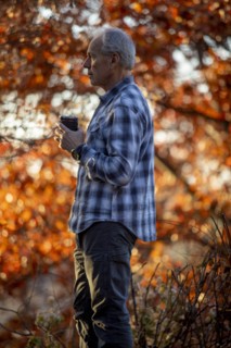 Man holding coffee cup by autumn trees
