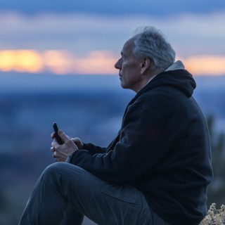 Seated man holding smart phone at sunset