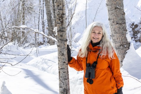 Mature woman wearing orange coat by bare trees in snow