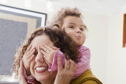 Girl with her hands covering her mother's eyes