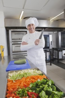 Smiling chef holding kitchen knife by raw vegetables