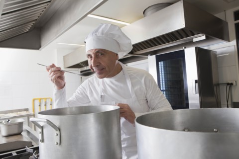 Smiling chef tasting food from pot