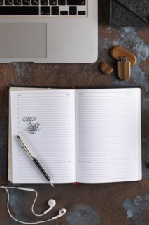 Open notebook by laptop with earbuds and USB stick
