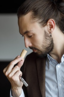 Young man smelling wine on cork at tasting