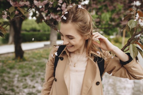 Smiling woman among falling petals from tree in bloom