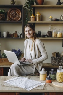 Smiling young woman using laptop in kitchen
