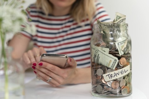 Woman using smart phone by travel saving jar