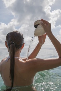 Woman in sea pouring water out of nautilus seashell