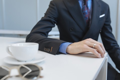 Man wearing suit leaning on table by tea cup and sunglasses