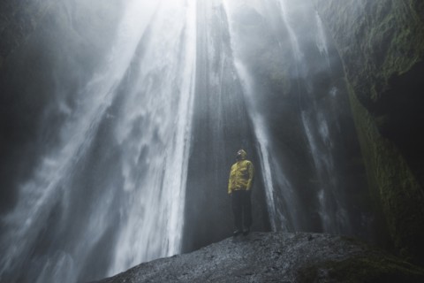 Man wearing yellow raincoat by Seljalandsfoss waterfall in Iceland