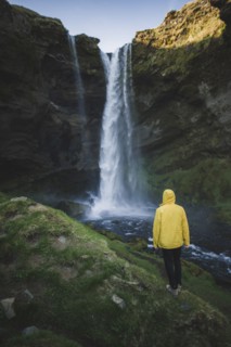 Man wearing yellow raincoat by Kvernufoss waterfall in Iceland