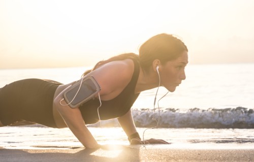 Woman wearing headphones doing push-up on beach