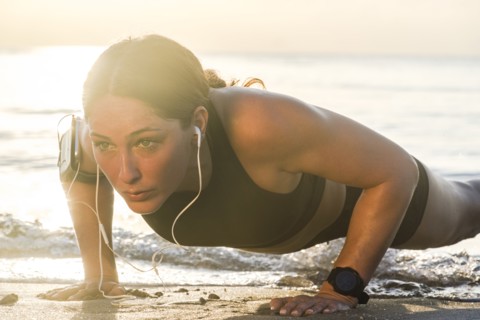 Woman wearing headphones doing push-up on beach