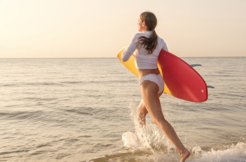 Woman holding surfboard running into sea