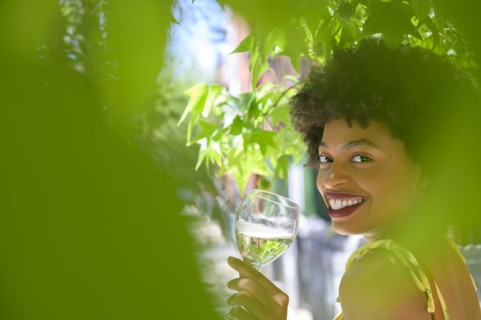 Smiling young woman with glass of white wine under tree