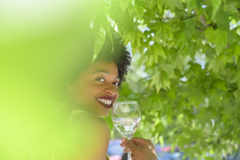 Smiling young woman with glass of white wine under tree