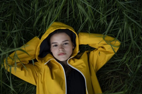 Teenage girl wearing yellow raincoat lying on grass