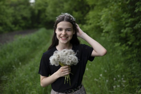 Smiling teenage girl holding dandelions in a field