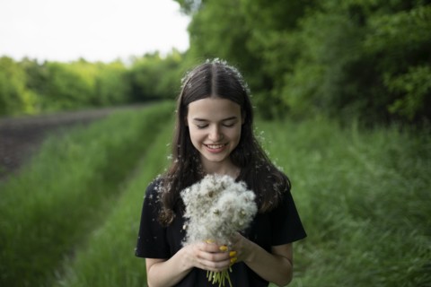Smiling teenage girl holding dandelions in a field
