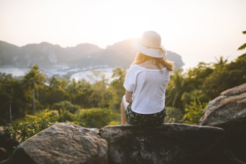 Woman wearing straw hat sitting on rock at sunset on Phi Phi Islands, Thailand