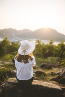 Woman wearing straw hat sitting on rock at sunset on Phi Phi Islands, Thailand