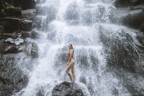 Woman wearing red swimsuit by waterfall in Bali, Indonesia