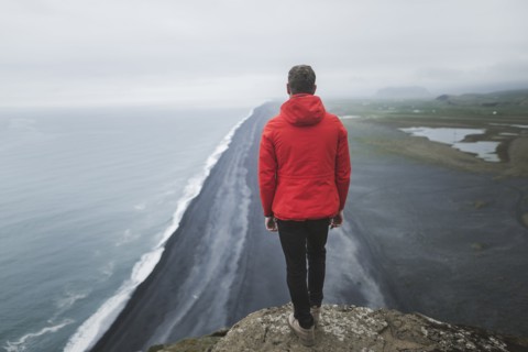 Man wearing red coat above beach in Vik, Iceland