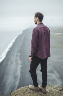 Man wearing purple shirt above beach in Vik, Iceland