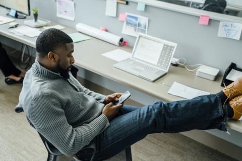 Man with his feet up using smart phone in office