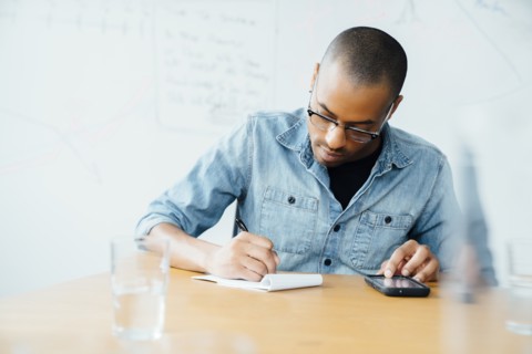 Man using smart phone while writing on note pad