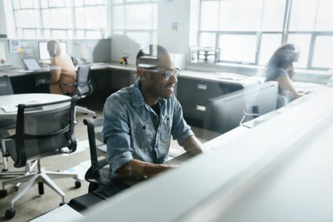 View through window of smiling man using computer in office