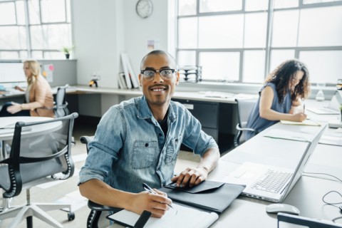 Smiling man using note pad by laptop in office