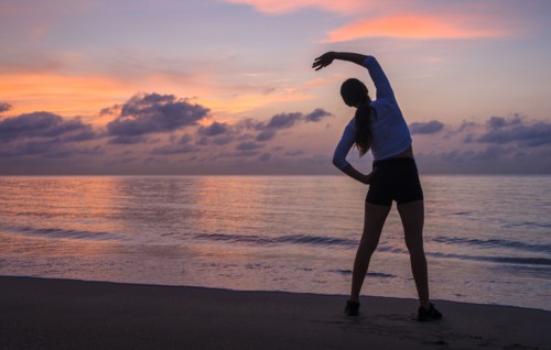 Woman practicing yoga on beach at sunset