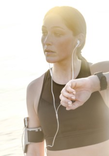 Woman wearing headphones checking wrist watch on beach